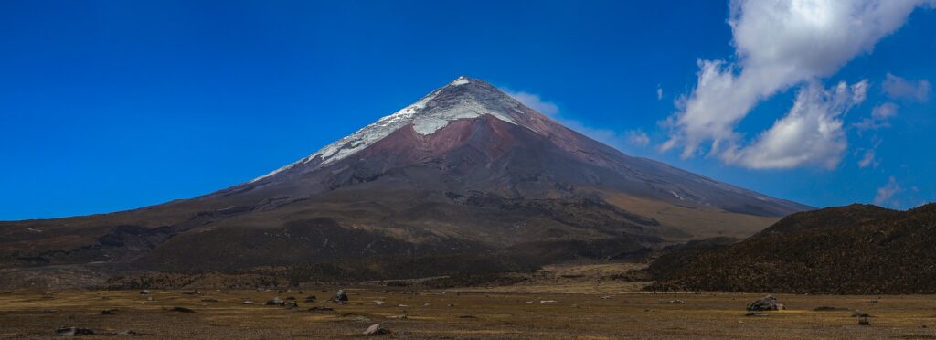 wulkan cotopaxi w ekwadorze - widok na całość, niebieskie niebo z chmurami i ośnieżonym szczytem.