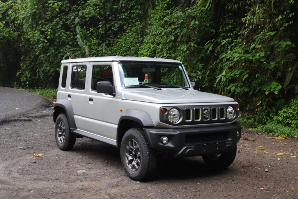 zdjęcie przedstawiające Suzuki Jimny srebrny. W tle widać gęstą zieleń intensywną 